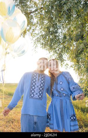 Glückliches Paar lächelt, umarmt sich und hält Luftballons während des Spaziergangs auf der Wiese. Sie sind in ukrainische nationale bestickten Hemden gekleidet. Stockfoto