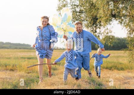 Glückliche Eltern mit zwei Zwillingssöhnen haben Spaß und laufen mit Luftballons auf der Wiese. Sie sind in ukrainische nationale bestickten Hemden gekleidet. Schließen Stockfoto