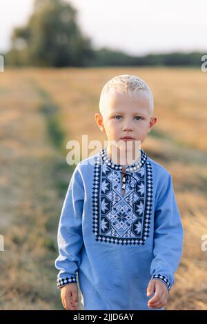 Porträt des blonden ukrainischen Jungen auf der Wiese während des Spaziergangs. Er ist in einem ukrainischen Nationalhemd bestickt. Stockfoto