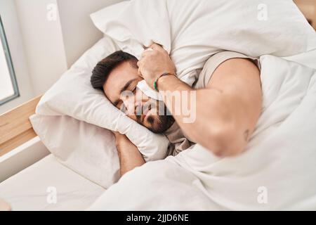 Junger hispanischer Mann, der auf dem Bett liegt und Schlaflosigkeit wegen Lärm im Schlafzimmer leidet Stockfoto