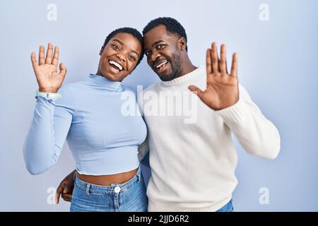 Das junge afroamerikanische Paar steht auf blauem Hintergrund und wagt es, fröhlich und lächelnd willkommen zu heißen Stockfoto