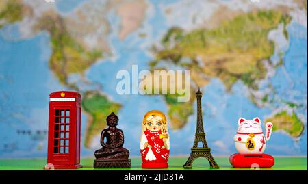 Souvenirs aus der ganzen Welt auf dem Hintergrund der Weltkarte. Rote Londoner Kabine, Statue von Buddha, russische Puppe Matroschka, Eiffelturm, Maneki Stockfoto