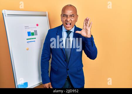 lateinischer Mann mittleren Alters, der Geschäftskleidung auf der Karte trägt, schreit laut und schreit laut zur Seite mit der Hand am Mund. Kommunikationskonzept. Stockfoto