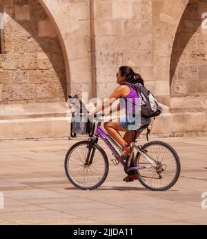 Frau auf dem Fahrrad / Fahrrad mit einem Hund in einem Korb auf der Vorderseite ihres Fahrrads auf der plaza Maria in der spanischen Stadt Burgos Spanien Stockfoto