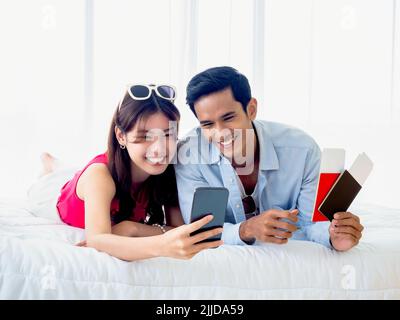Glückliches asiatisches Paar mit Handy. Junge Männer und Frauen in zwangloser Atmosphäre fühlen sich glücklich mit einem Lächeln und dem Blick auf den Smartphone-Bildschirm, während sie den Pass halten Stockfoto