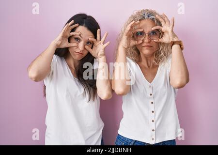 Mutter und Tochter stehen zusammen auf rosa Hintergrund versuchen, die Augen mit den Fingern zu öffnen, müde und müde für die morgendliche Müdigkeit Stockfoto