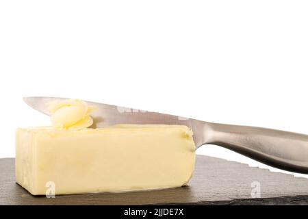 Zwei Butterstücke mit einem Metallmesser auf einem Schieferstein, Nahaufnahme, isoliert auf weißem Hintergrund. Stockfoto