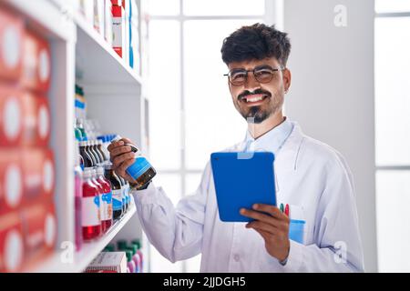 Der junge hispanic-Mann Apotheker organisiert die Regale mit dem Touchpad in der Apotheke Stockfoto