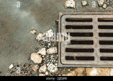 Wasser fließt aus der Ablaufluke. Kanalisation Brunnen von Abwasser. Unfall in der Abwasseranlage. Schmutzige Abwässer fließen auf der Straße. Abflusssystem für was Stockfoto