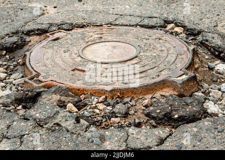 Kanalloch auf einer alten, kaputten Asphaltstraße. Straßenarbeiten Stockfoto