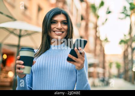 Junge hispanische Frau, die Smartphone benutzt und eine Tasse Kaffee in der Stadt trinkt Stockfoto