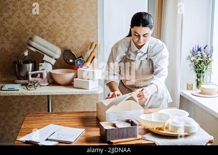 Weibliche Bäckerin, Konditorei bereitet Kuchen zu bestellen. Arabisch asiatische Frau Kuchen für Online-Lieferung Stockfoto