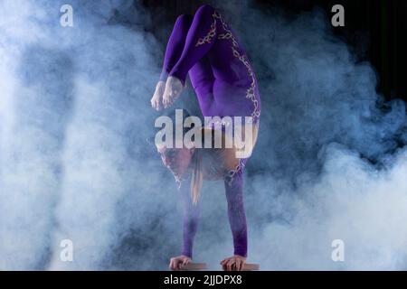 Ein akrobatin führt einen schönen Zirkustrick in Puffs aus purpurem Rauch durch. Stockfoto