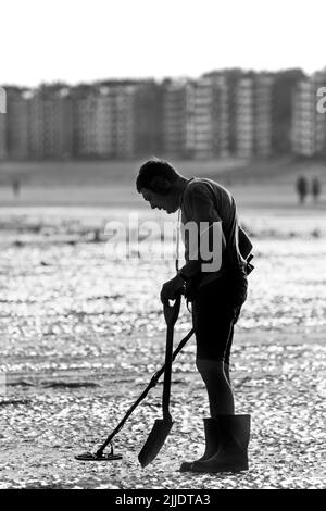 Mann mit Metalldetektor, der an einem frühen Morgen im Sommer während der Ferienzeit am Sandstrand entlang der Nordseeküste strandkämmt Stockfoto