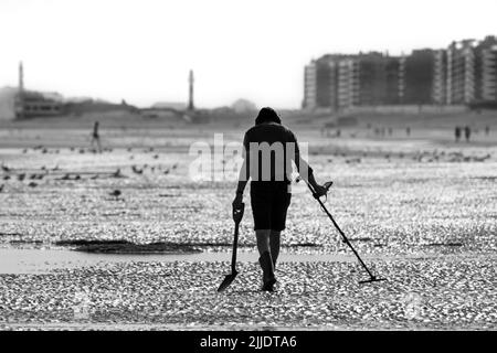 Mann mit Metalldetektor, der an einem frühen Morgen im Sommer während der Ferienzeit am Sandstrand entlang der Nordseeküste strandkämmt Stockfoto