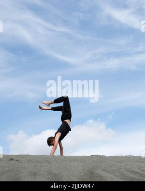 Der junge Mann steht am Horizont auf Händen am Sand in der Wüste Stockfoto