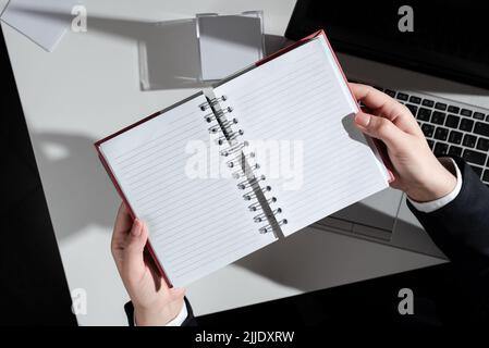 Frau Hält Notizbuch Mit Neuen Ideen Über Dem Schreibtisch Mit Notizen Und Lap Top. Stockfoto