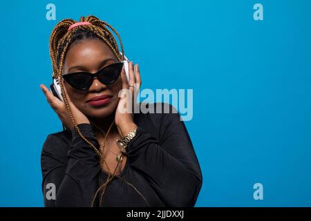 Eine Frau mit Sonnenbrille blickt in die Kamera, während sie Musik hört. Stockfoto