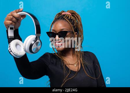 Eine junge dunkelhäutige Frau hält kabellose Kopfhörer in der Hand. Stockfoto