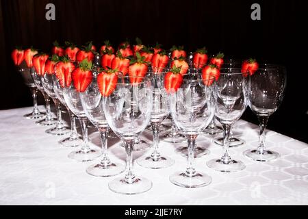 Reihen von Sektgläsern, die mit roten Erdbeeren am Buffettisch dekoriert sind. Serviert wird ein Buffettisch mit Gläsern und Erdbeeren. Catering und Bedienung Stockfoto