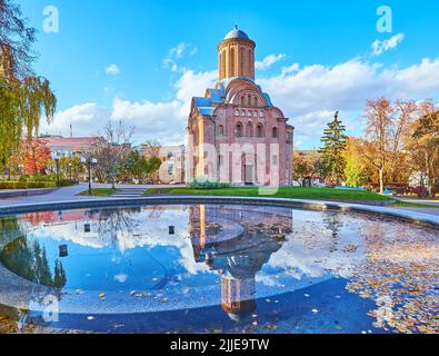 Auf der Oberfläche des Brunnens im Bohdan Khmelnyzki Park, Tschernihiw, Ukr spiegeln sich die rote Backsteinkirche St. Paraskeva (Pjatnyzka) und der strahlend blaue Himmel Stockfoto