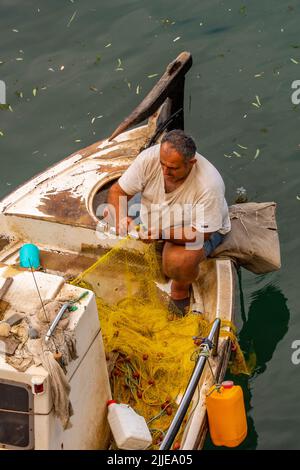 griechischer Fischer auf der Insel kreta flicken Netze auf seinem Boot in einem Hafen im Abendlicht, griechischer Fischer im Boot reparieren Ausrüstung für morgen Stockfoto