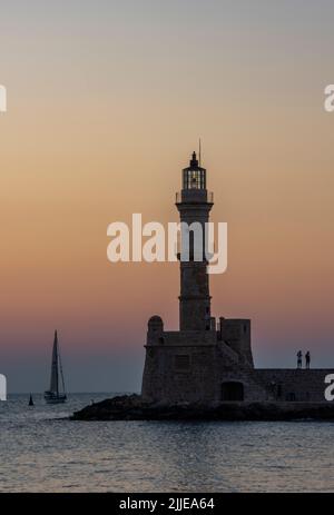 yacht, die bei Sonnenuntergang in den Hafen einfährt, vorbei am Hsitoric Leuchtturm in chania auf der griechischen Insel kreta, Sonnenuntergang über dem Leuchtturm in chania. Stockfoto