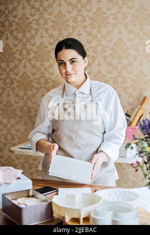 Weibliche Bäckerin, Konditorei bereitet Kuchen zu bestellen. Arabisch asiatische Frau Kuchen für Online-Lieferung Stockfoto