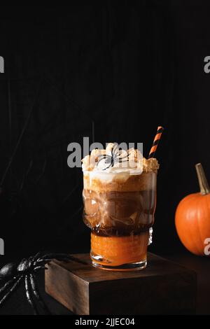 Halloween Kürbis Gewürzkaffee Latte verzierte Spinne und Popcorn in stilvollem Glas als Möwe auf schwarzem Hintergrund. Vertikales Format. Stockfoto