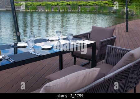 Leere Gläser, weiße Teller und Besteck auf einem Tisch in einem Strandrestaurant. Tischstimmung für ein festliches Abendessen. Stockfoto