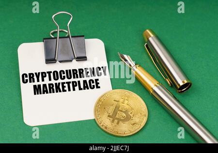 Kryptowährung und Geschäftskonzept. Auf einer grünen Fläche, einer Bitcoin-Münze, einem Stift und einem Blatt Papier mit der Aufschrift - Kryptowährungsmarkt Stockfoto