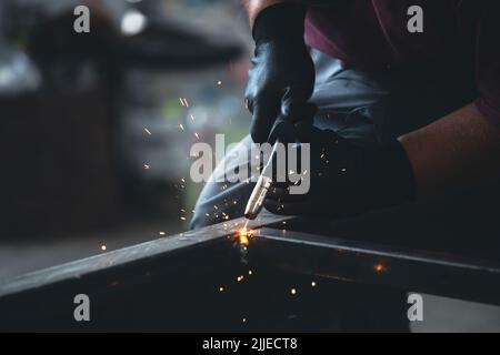 Der Handwerker, der an seinem Arbeitsplatz in der Werkstatt Schweißen und Schleifen durchführt, während die Funken um ihn herum „fliegen“. Er trägt einen Schutzhelm und Stockfoto