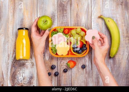 Mutter bereitet die Lunchbox für die Schule vor. Lunchbox mit gesunden Sandwiches, Saft, Beeren und Snacks. Zurück zum Schulhintergrund Stockfoto