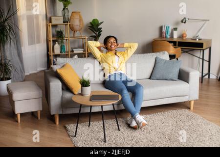 Schwarze Frau Hält Die Hände Hinter Dem Kopf Und Sitzt Entspannt Zu Hause Stockfoto