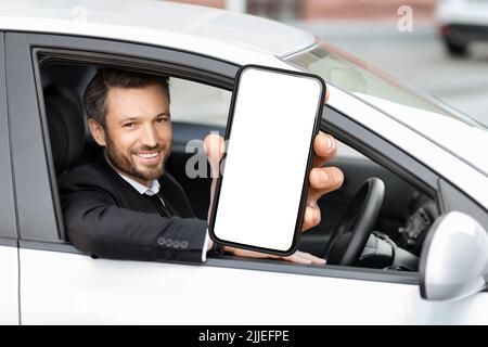 Fröhlicher Geschäftsmann sitzt im Auto, zeigt Handy, Nachbau Stockfoto