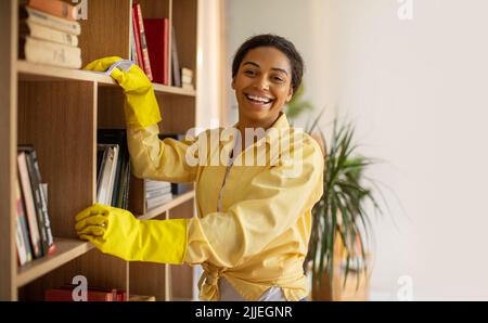 Afrikanische Frau Staubwischen Und Reinigung Bücherregal Mit Rag Zu Hause Stockfoto