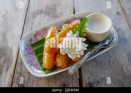 Thailändisches Dessert, Süße Bananen servieren mit Kokosnusssirup auf dem Teller und Holztisch. Stockfoto