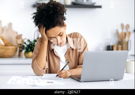 Überarbeitete junge afroamerikanische Frau, Freiberuflerin oder Studentin, die von zu Hause aus arbeitet, müde von langweiliger Online-Arbeit oder Studium, an chronischer Müdigkeit leidet, überfordert ist, schläft am Schreibtisch ein Stockfoto