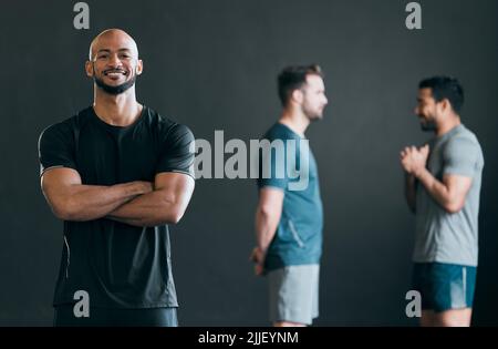 Es ist toll, Gleichgesinnte hinter jungen Leuten zu haben. Ein beschnittenes Porträt eines hübschen jungen Athleten, der mit gekreuzten Armen mit seinen Freunden steht Stockfoto
