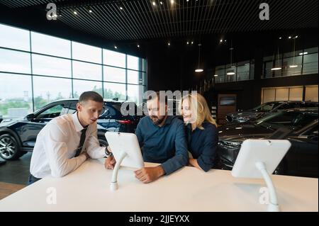 Kaukasisches Ehepaar wählt ein Auto in einem Autohaus auf digitalen Tablets. Stockfoto