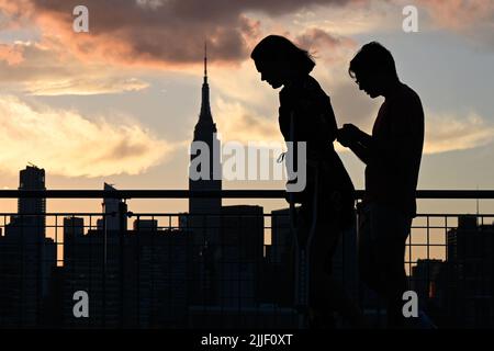 Auf dem Spaziergang entlang der Uferpromenade im Stadtteil Greenpoint in Brooklyn, New York, werden die Menschen vor der Skyline von Manhattan geschildet. Stockfoto