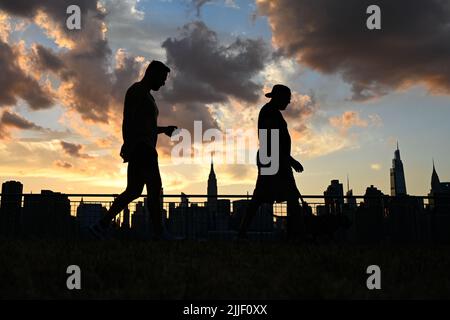 Auf dem Spaziergang entlang der Uferpromenade im Stadtteil Greenpoint in Brooklyn, New York, werden die Menschen vor der Skyline von Manhattan geschildet. Stockfoto