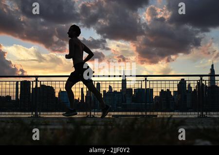 Auf dem Spaziergang entlang der Uferpromenade im Stadtteil Greenpoint in Brooklyn, New York, werden die Menschen vor der Skyline von Manhattan geschildet. Stockfoto