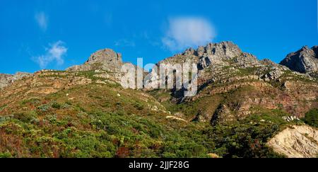 Blick von unten auf majestätische Berge mit Büschen, Grün und wolkig blauen Himmel kopieren Raum oben. Naturlandschaft von Bergfelsen Aufschlüsse mit wilden Stockfoto