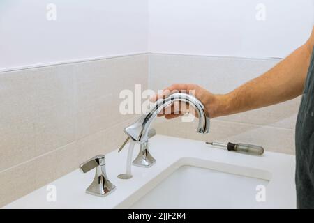 Ein Klempner bei der Arbeit montiert und installiert einen Wasserhahn im Badezimmer seines Kunden Stockfoto