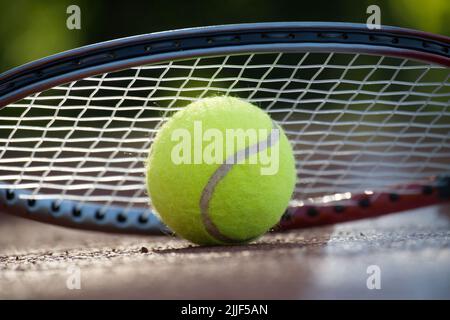 Nahaufnahme der Tennisrakete über dem gelben Tennisball auf Hartplätzen in der niedrigen Ansicht Stockfoto