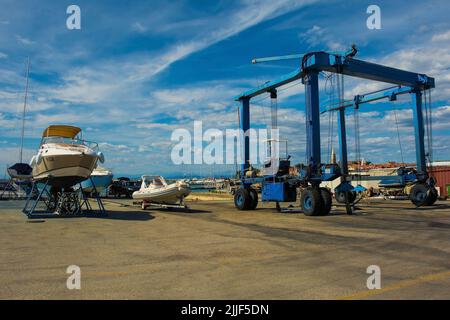 Izola, Slowenien - 9.. Juli 2022. Ein fahrbarer Hängeschiff oder Hebezeug und ein kleines Freizeitboot, das auf einer Bootsanlegestelle am Yachthafen von Izola repariert wird Stockfoto