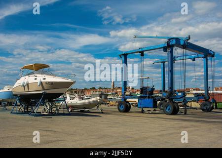 Izola, Slowenien - 9.. Juli 2022. Ein fahrbarer Hängeschiff oder Hebezeug und ein kleines Freizeitboot, das auf einer Bootsanlegestelle am Yachthafen von Izola repariert wird Stockfoto