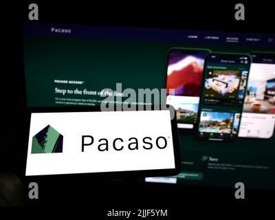 Person, die Mobiltelefon mit dem Logo des US-Immobilienunternehmens Pacaso auf dem Bildschirm vor der Business-Webseite hält. Konzentrieren Sie sich auf die Telefonanzeige. Stockfoto