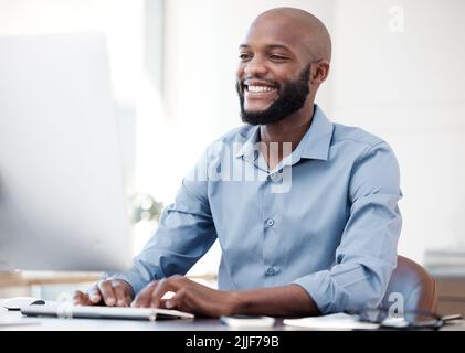 HES macht Fortschritte. Ein hübscher junger Geschäftsmann, der im Büro an seinem Computer arbeitet. Stockfoto
